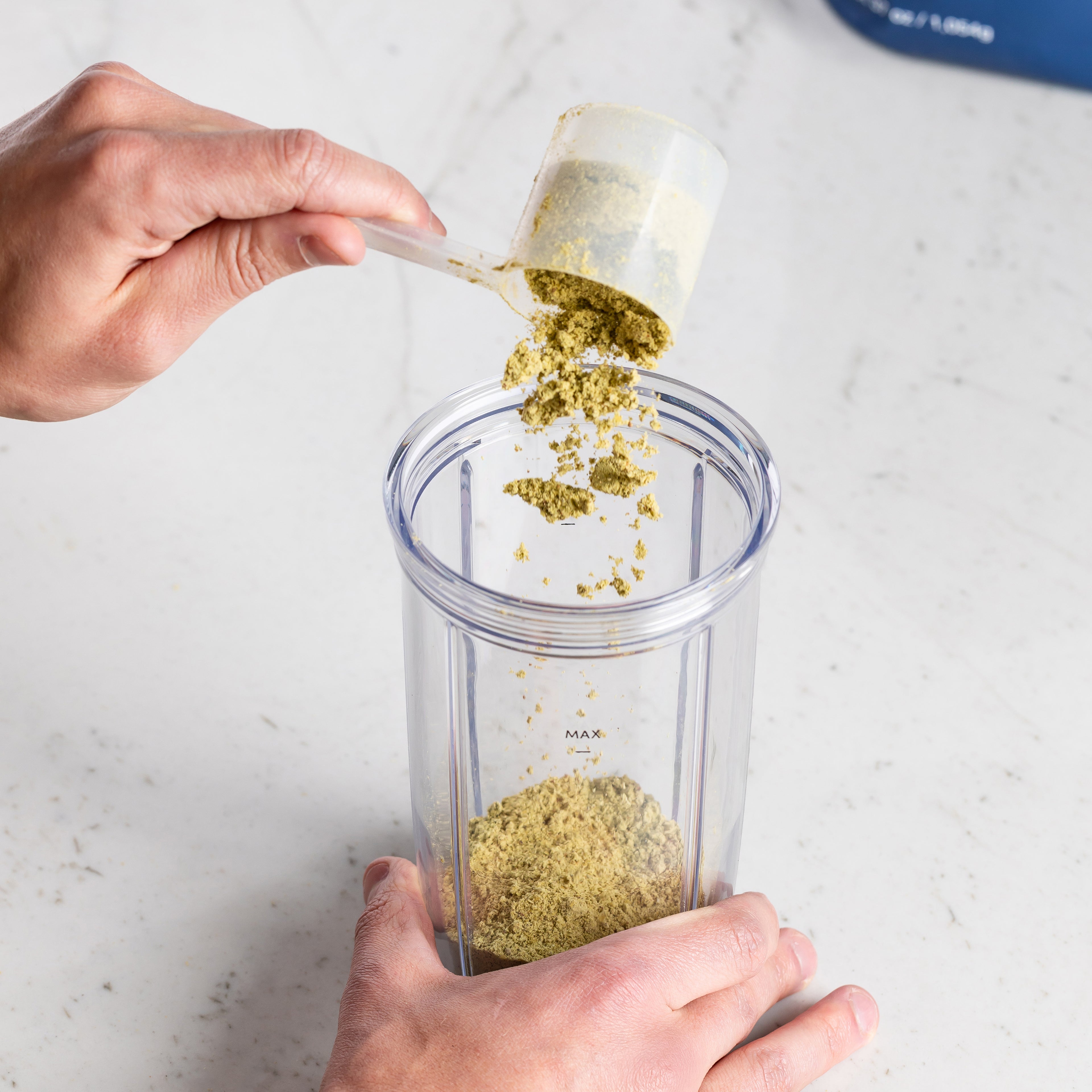 Person Field Theory powder to a clear blender container on a marble surface