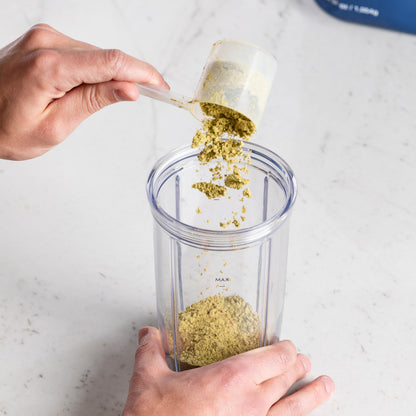 Person Field Theory powder to a clear blender container on a marble surface