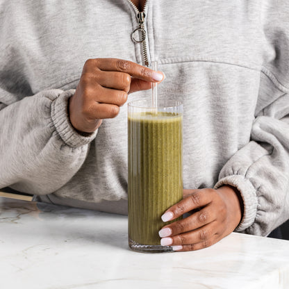 Person holding a glass of freshly blended shake with a straw on a light background